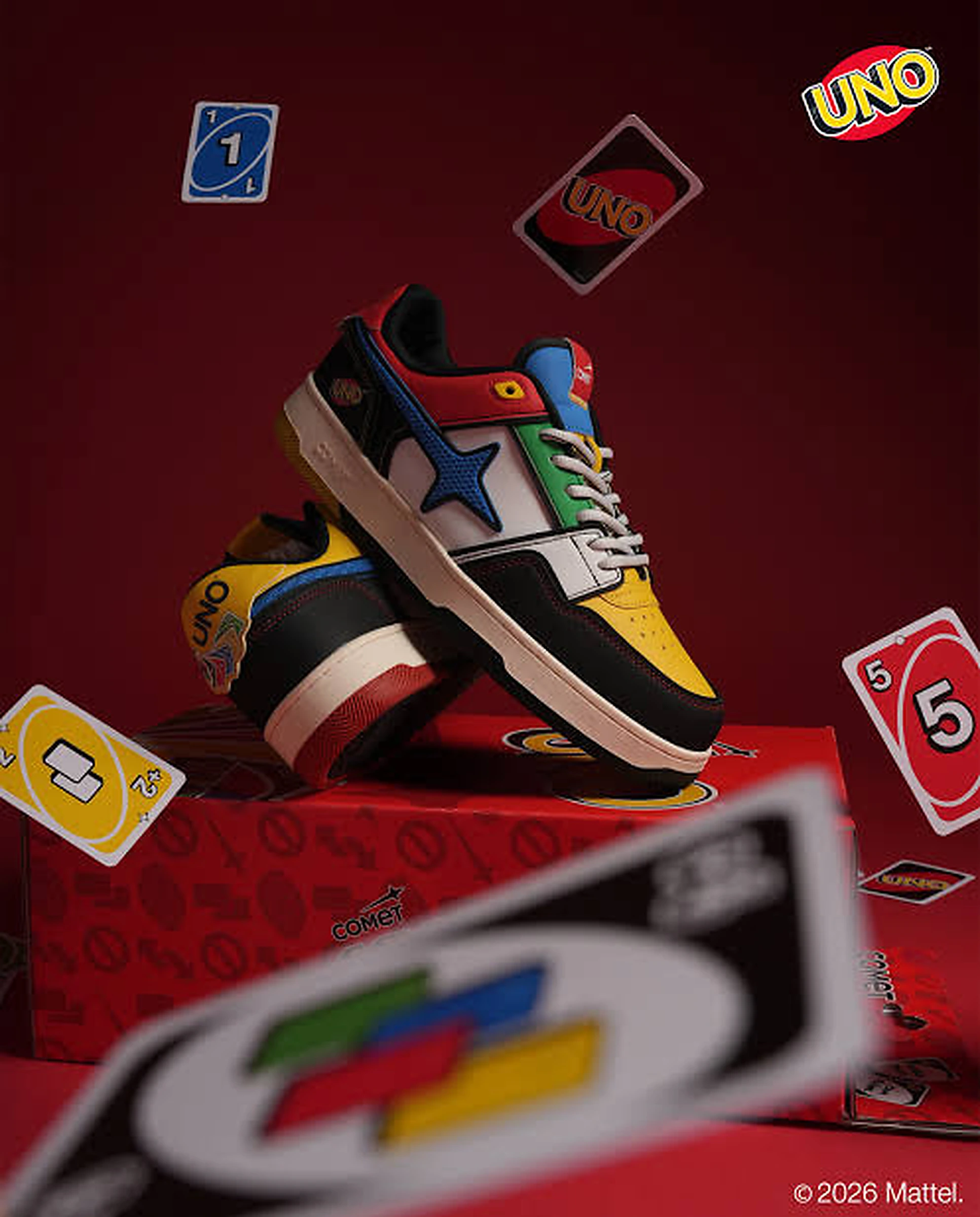 Tenis UNO x COMET con paneles rojo, amarillo, azul y verde sobre una caja roja rodeada de cartas de UNO